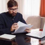 entrepreneur in eyeglasses works with a laptop and reviews documents