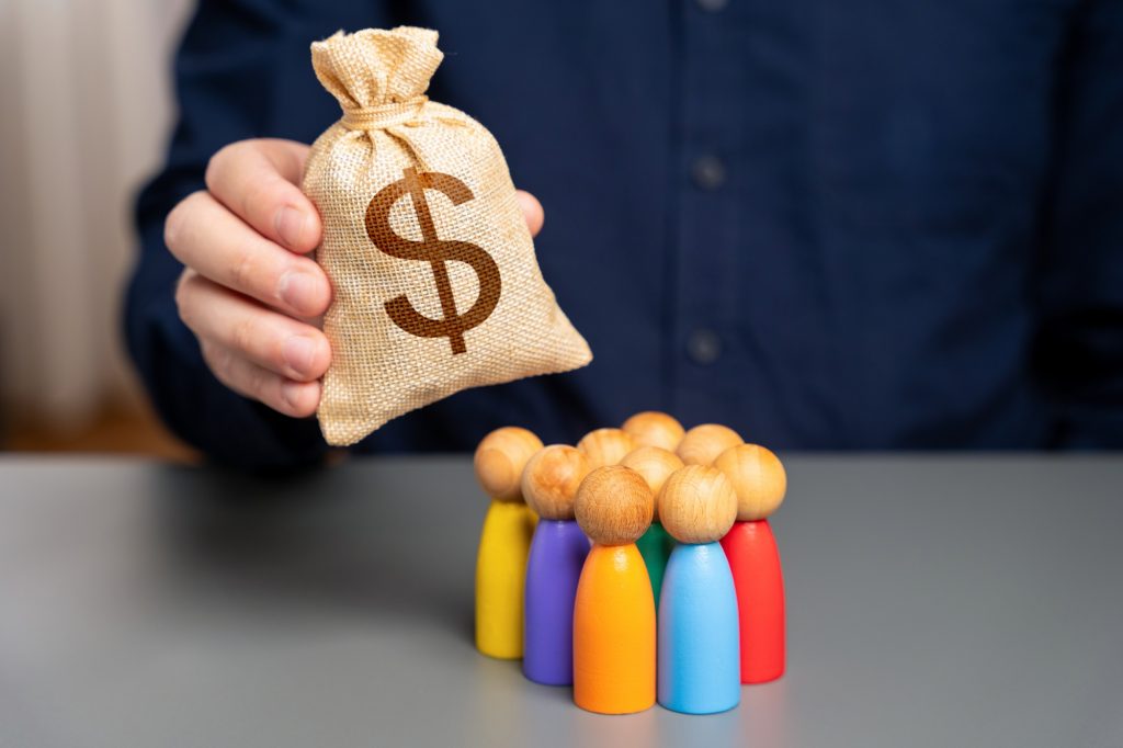 Businessman holding dollar money bag over group of people figurines.